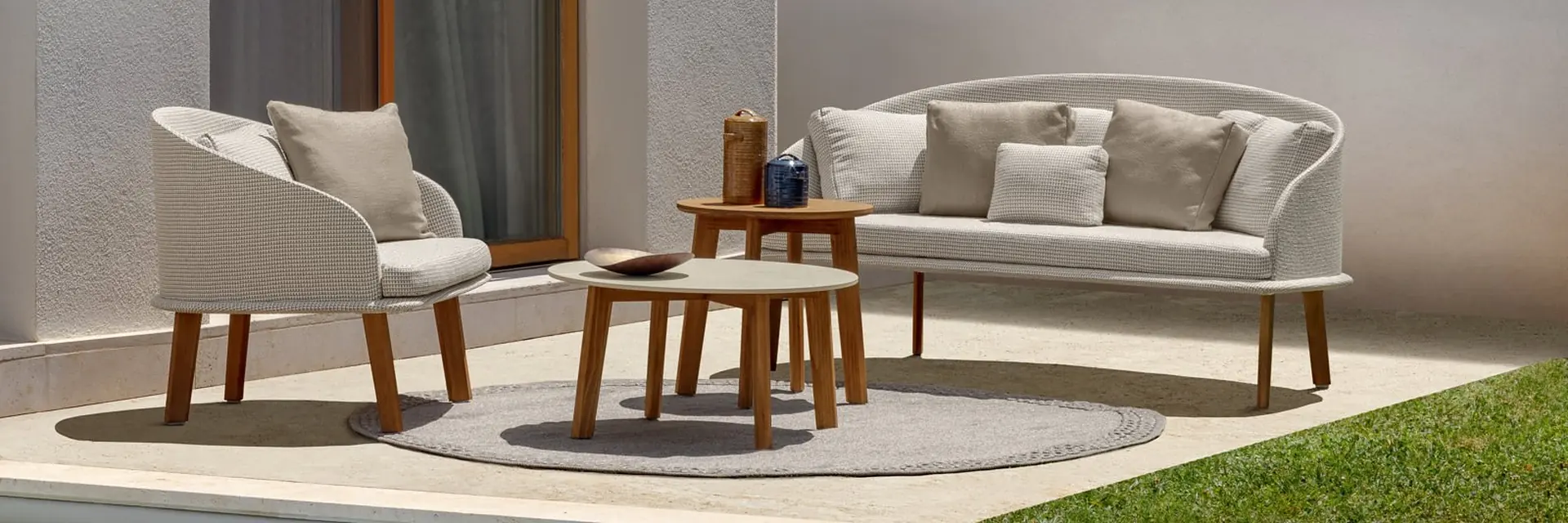 Talenti Cleo sofa and armchair with woven shells and teak legs around two low tables on a stone terrace