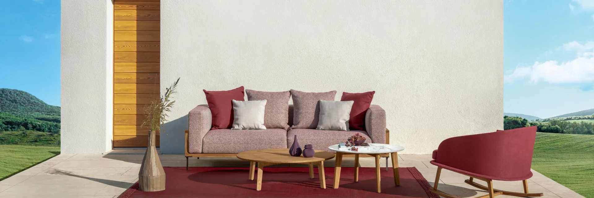 Talenti Cleo three-seater sofa with burgundy cushions, low tables and a red rocking chair on a red rug, in front of a white wall with a timber door