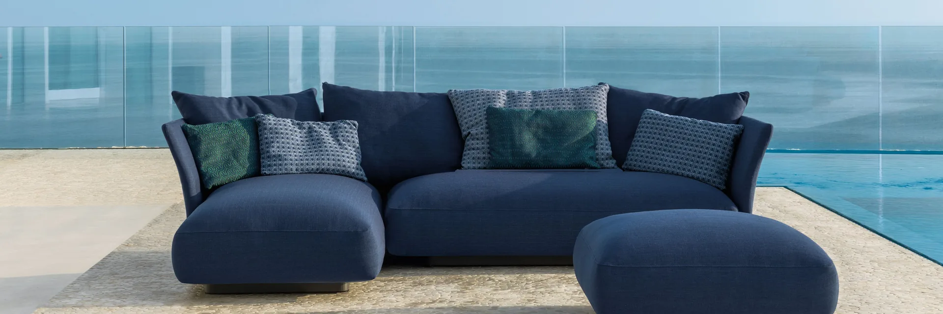 Talenti Cliff modular sofa in deep blue fabric on a pale terrace with a glass balustrade and the sea behind