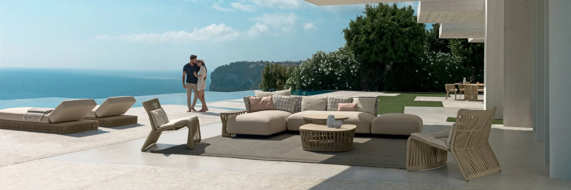 Talenti Cliff sofas and sun loungers on a terrace under a white canopy, with a couple looking out over the sea
