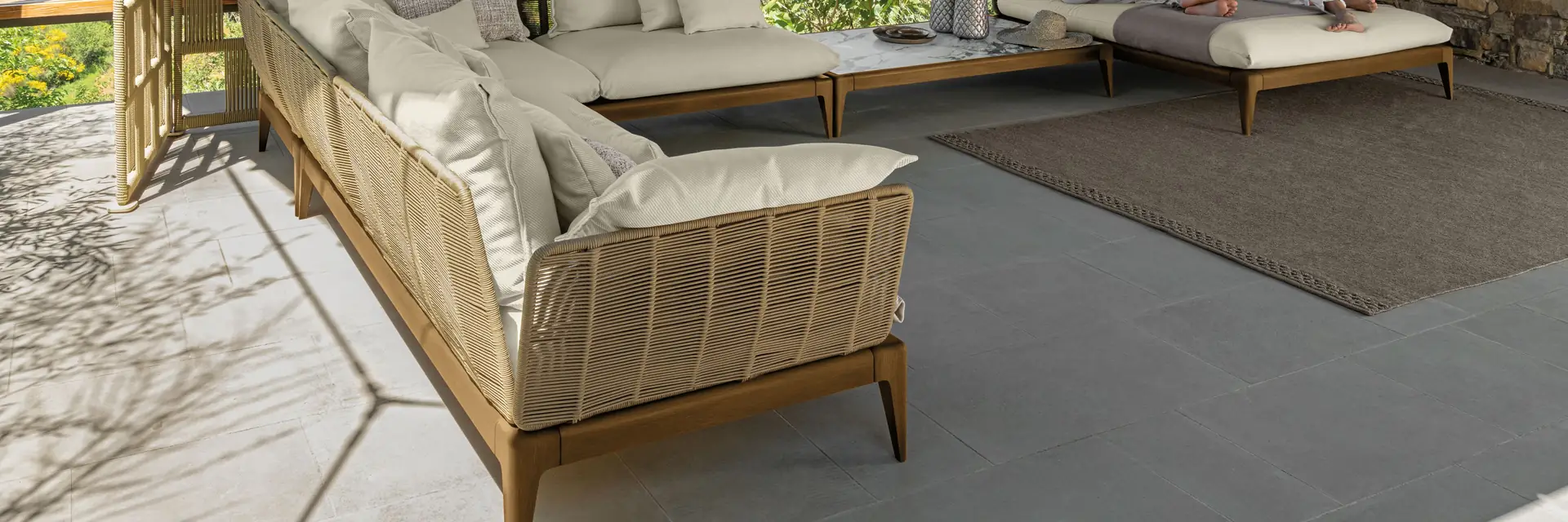 Talenti Cruise Teak corner sofa with woven sides and pale cushions on a terrace overlooking a green valley