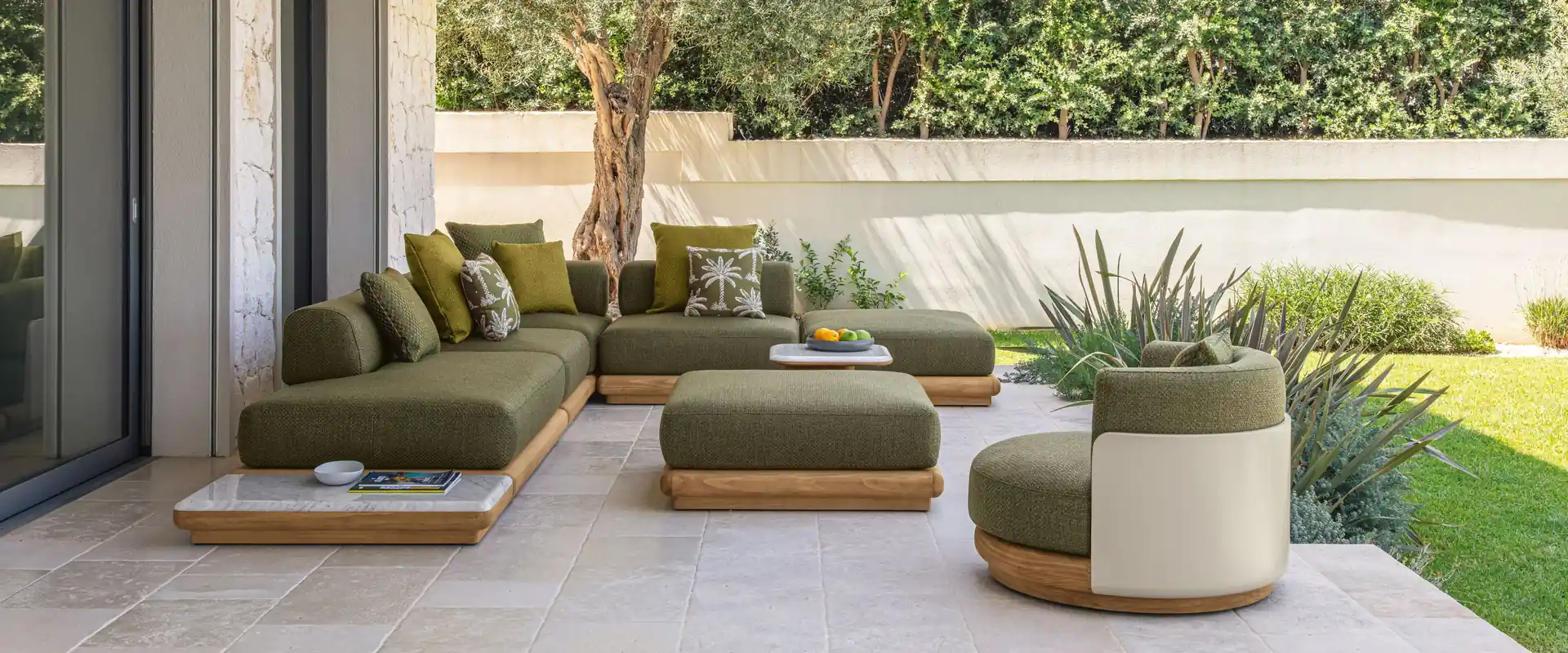 Talenti Itaca modular sofa in green fabric with poufs and a planter on a porch that opens onto a hedged garden