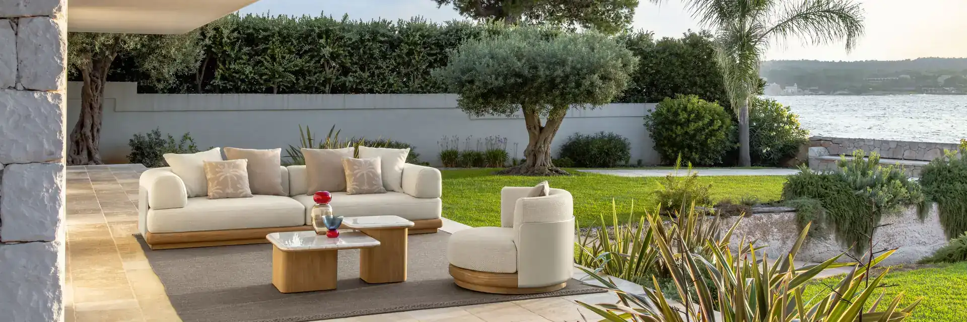 Talenti Itaca sofa and coffee table on a terrace beside a lawn with an olive tree and palms, overlooking the sea