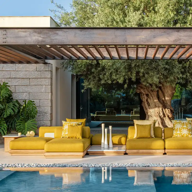 Talenti Itaca modular sofas in yellow fabric beside a pool, under a pergola with a large tree