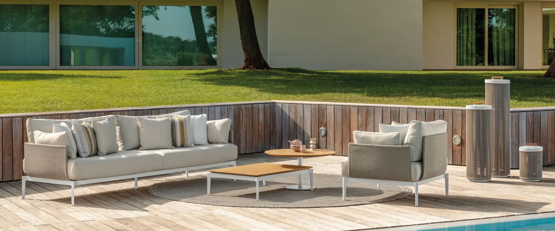 Talenti Leaf sofa and armchairs with striped cushions on a wooden deck by a pool, in front of a low modern house