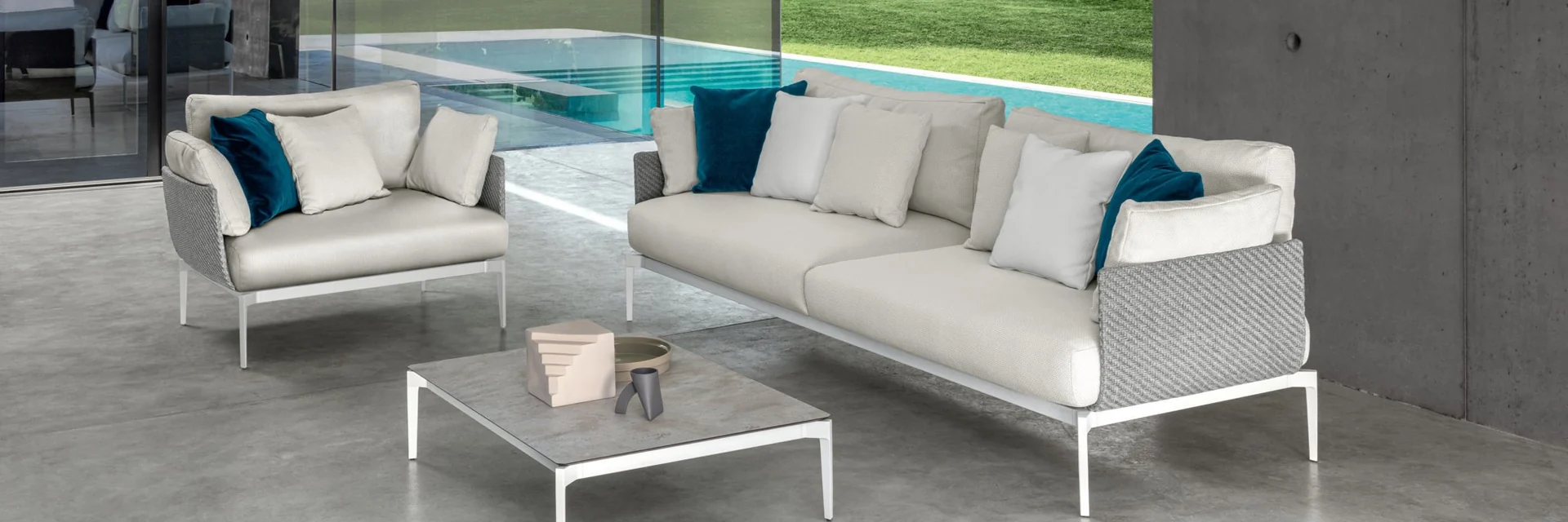 Talenti Leaf sofas with blue cushions and low tables on a terrace between a concrete wall and a pool