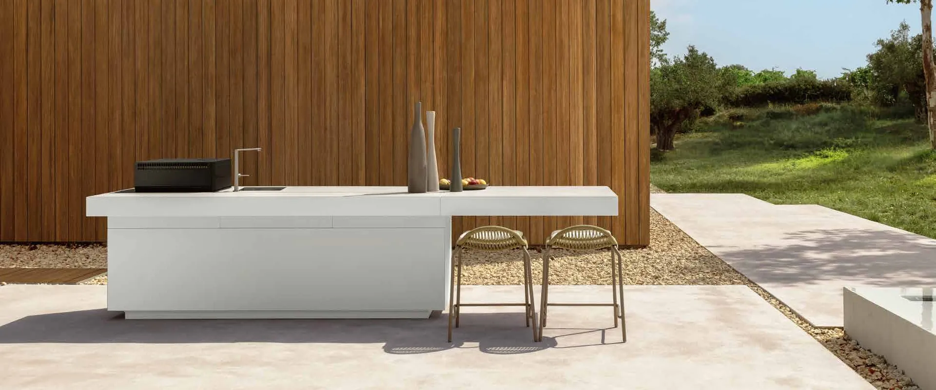 White Talenti outdoor kitchen island with bar stools in front of a timber wall, with olive trees and a meadow beyond