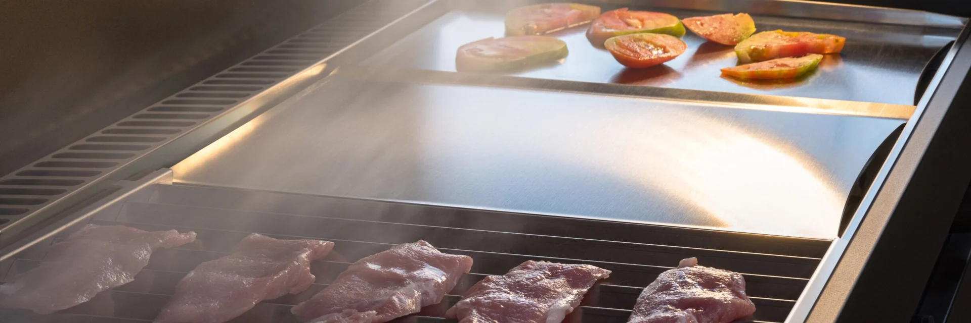 Steaks and vegetables on the grill of a Talenti Tikal outdoor kitchen in the evening light