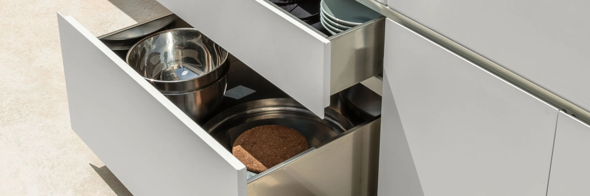 Open drawers with pans in a white Talenti Tikal outdoor kitchen island beside a pool