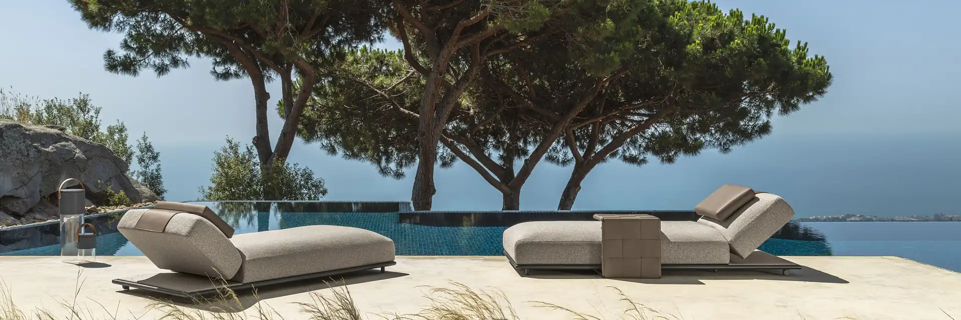 Talenti Tresse daybeds on a deck under a large umbrella pine, above the sea