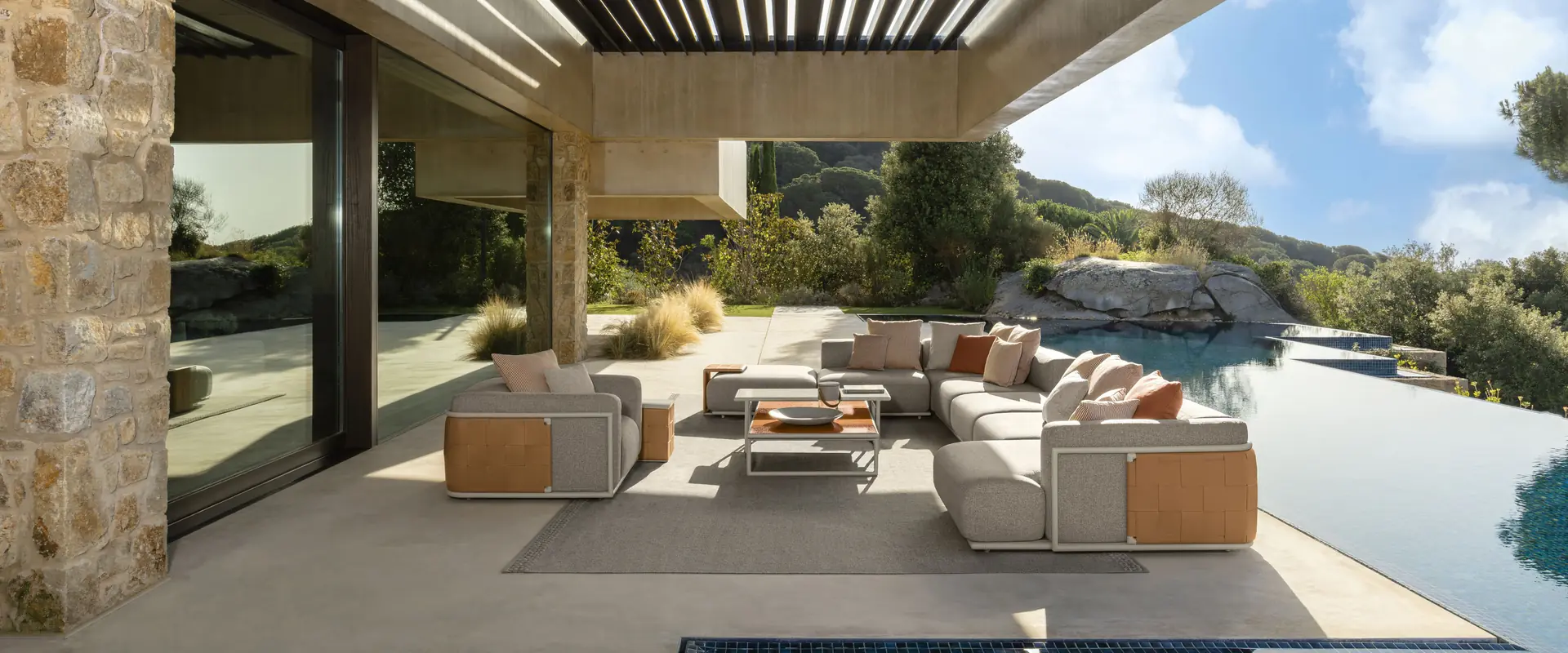 Talenti Tresse sofas and armchairs under a louvered pergola beside an infinity pool, with rocky hills beyond