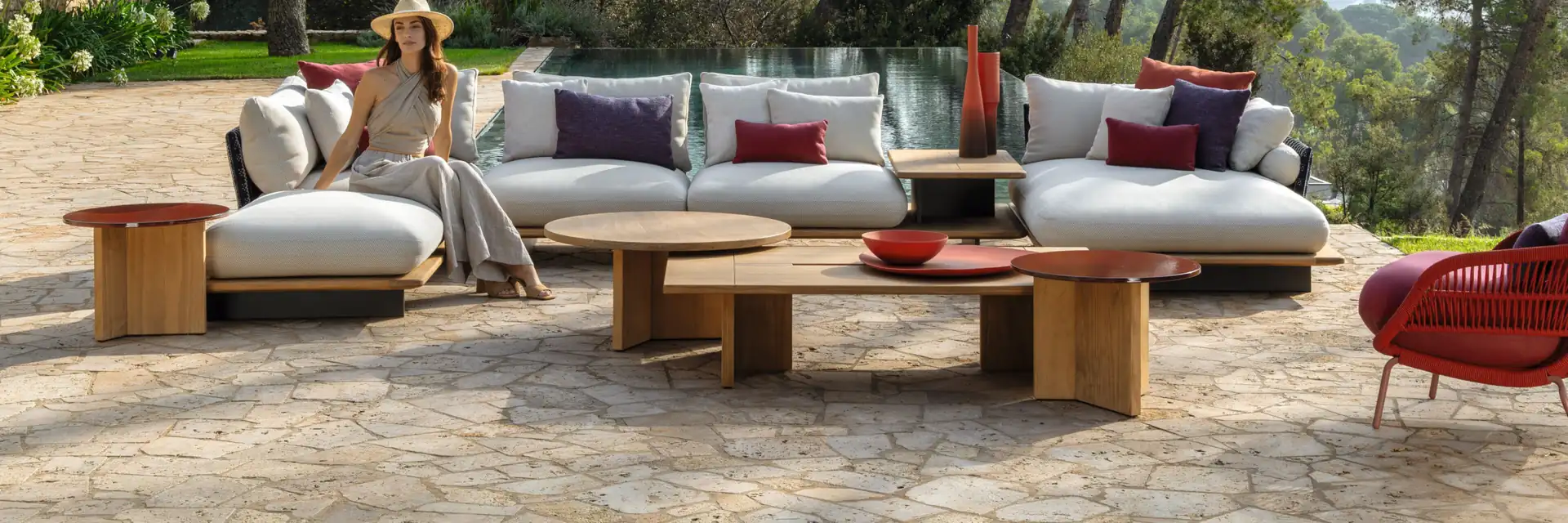 Talenti Venice sofas and low tables on a stone terrace among pine trees, with a woman in a sun hat sitting on one of them