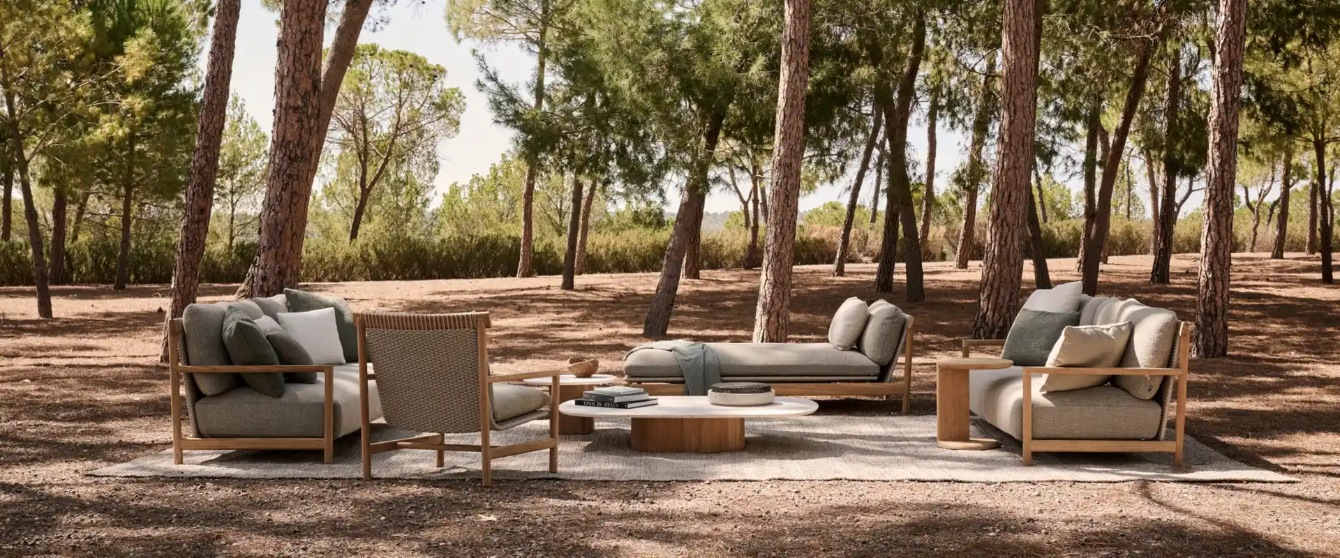 Tribù Amanu teak sofas, daybed and armchairs with green cushions set among pine trees on reddish earth