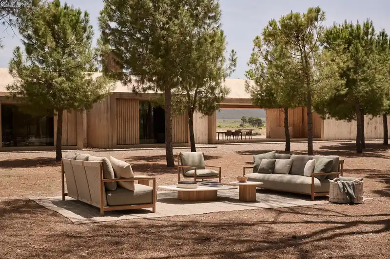 Tribù Amanu sofas and armchairs on a rug in front of a timber house, among pine trees