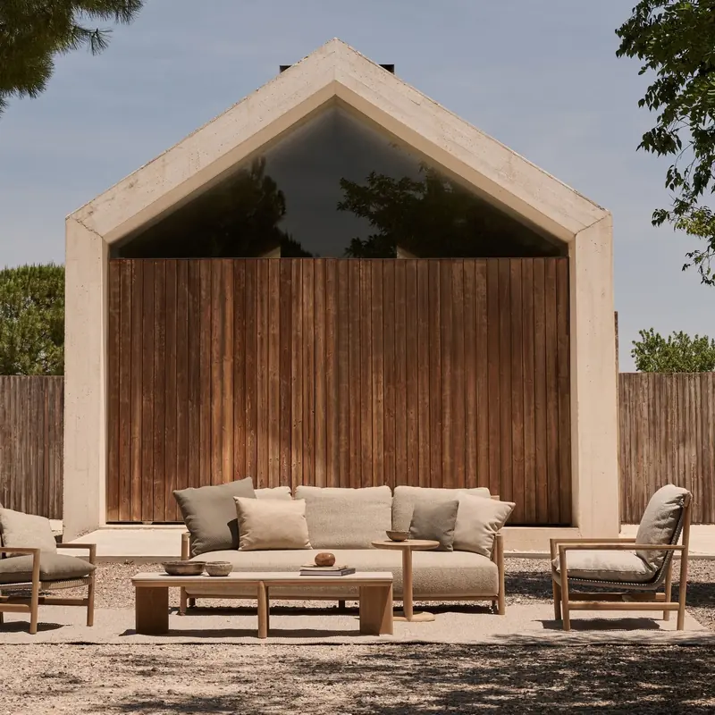 Tribù Amanu teak sofa, armchairs and coffee table before a gabled house clad in dark timber