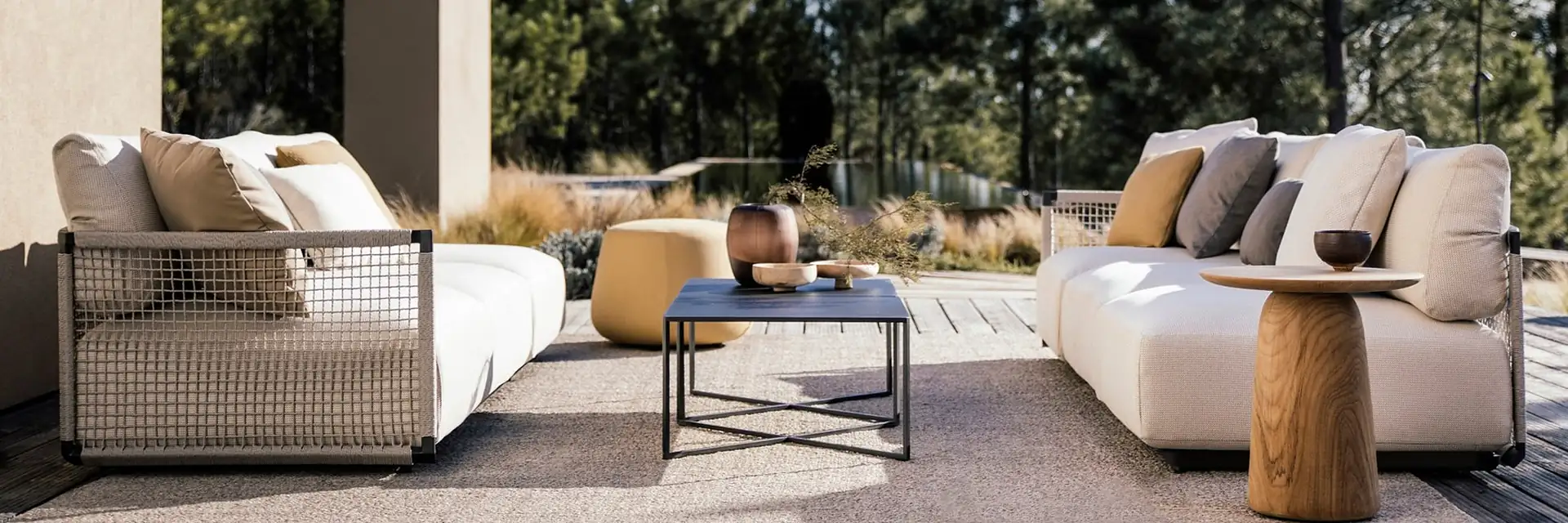 Tribù Dunes sofas and side tables on a timber deck in front of pine trees under a clear blue sky
