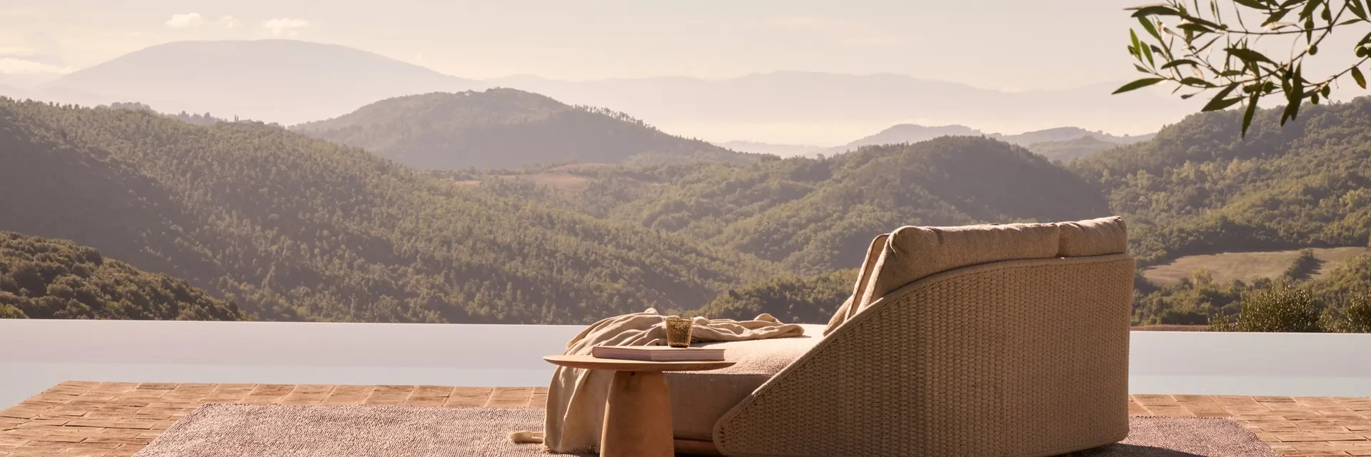 Tribù Elio lounge chair and side table on a terracotta terrace facing a range of misty hills