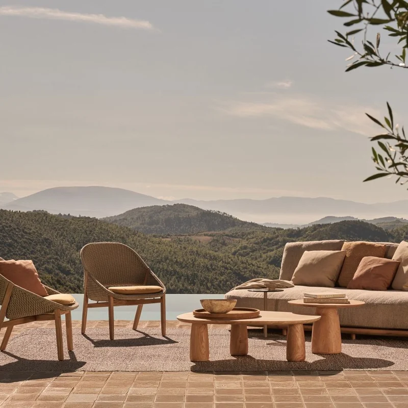 Tribù Elio lounge chairs, low tables and a sofa on a terracotta terrace by an infinity pool, hills in the haze