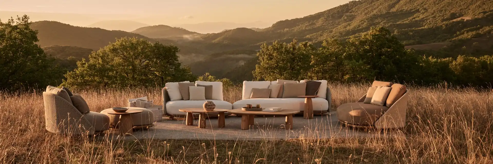 Tribù Elio sofas and low tables on a rug in a meadow, with hills in the evening light