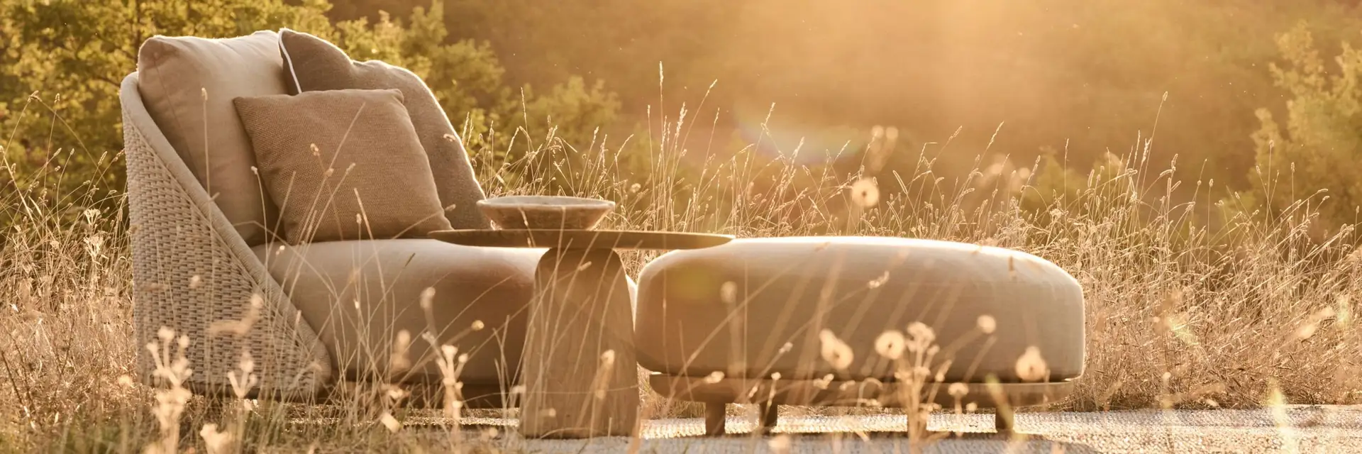 Tribù Elio sofa with a chaise end among dry grasses, with the sun setting over the hills
