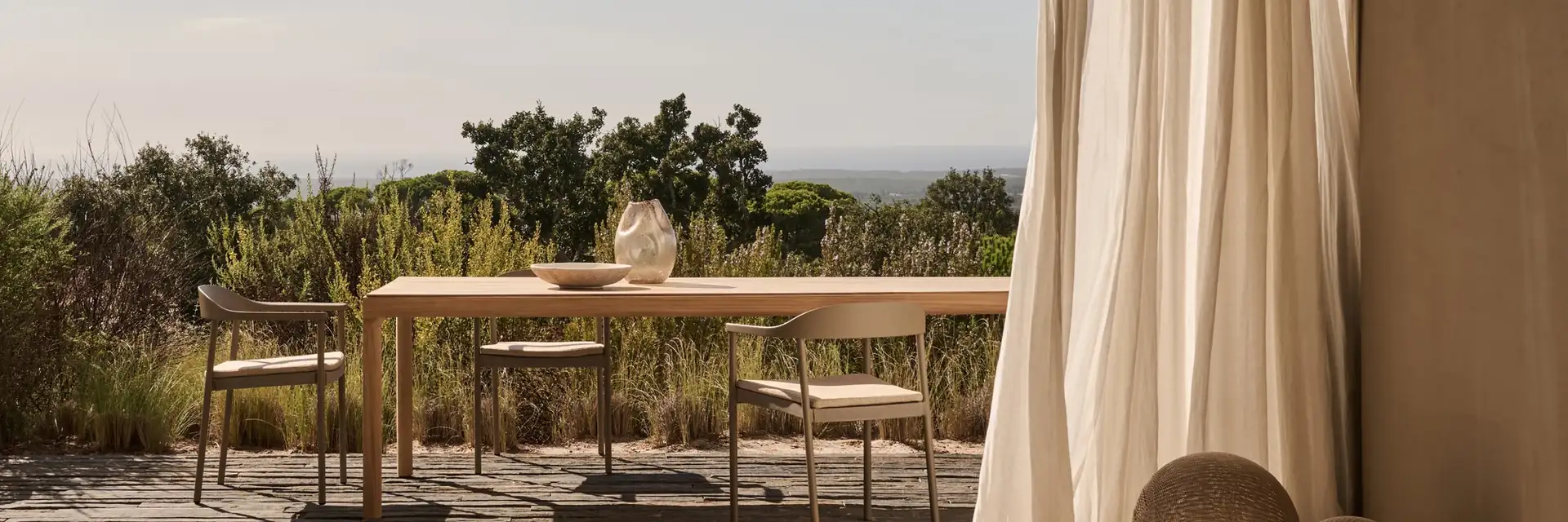 Tribù Illum dining table and chairs on a terrace seen from under a pitched roof with a linen curtain