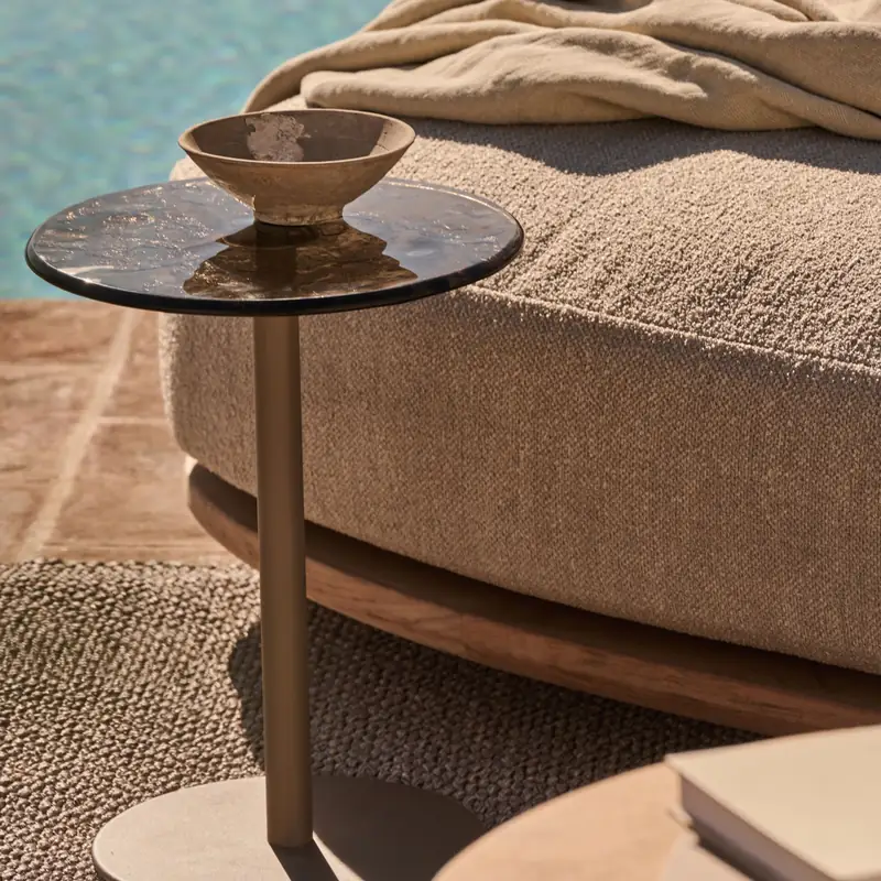 Tribù Mare side table with a tinted glass top and a ceramic bowl beside a daybed, with a pool behind