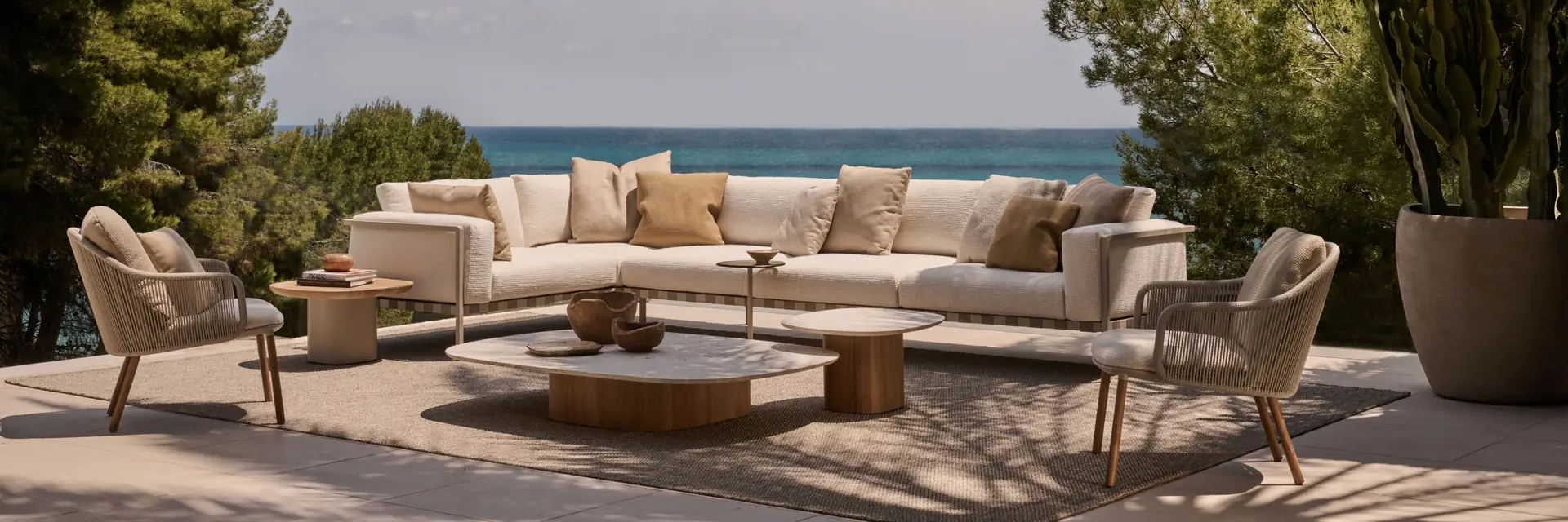 Tribù Mare modular sofa and low tables on a terrace surrounded by pines and palms, with the sea beyond