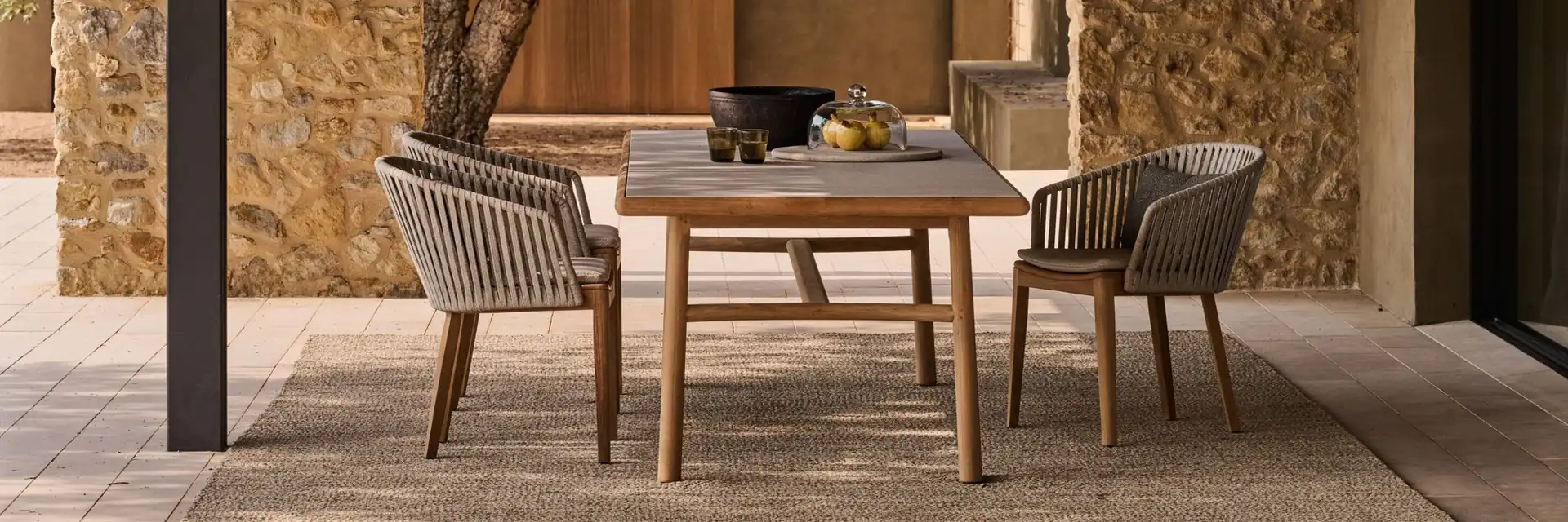 Tribù Mood rope dining chairs at a teak table on a terrace beside a stone wall