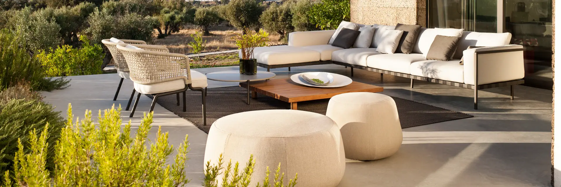 Tribù Natal Alu aluminium corner sofa with armchairs and round poufs on the terrace of a modern villa, surrounded by olive trees