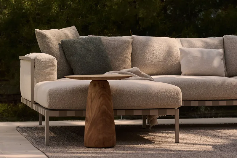 Tribù Natal Alu outdoor sofa with deep cushions and a round teak side table on a rug at dusk