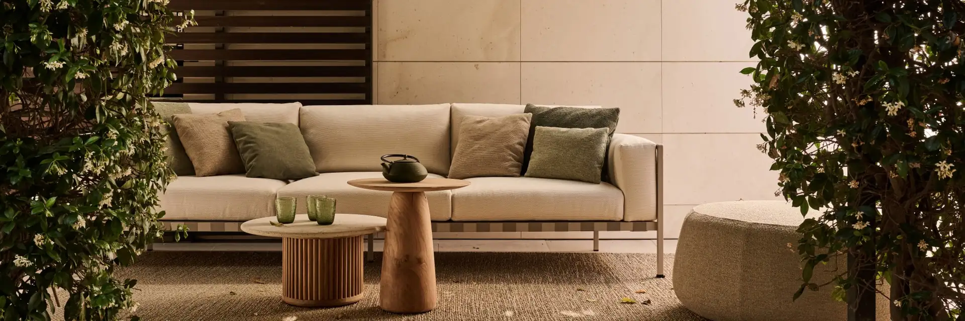 Tribù Natal Alu outdoor sofa with cushions and a round teak table in a courtyard with climbing plants