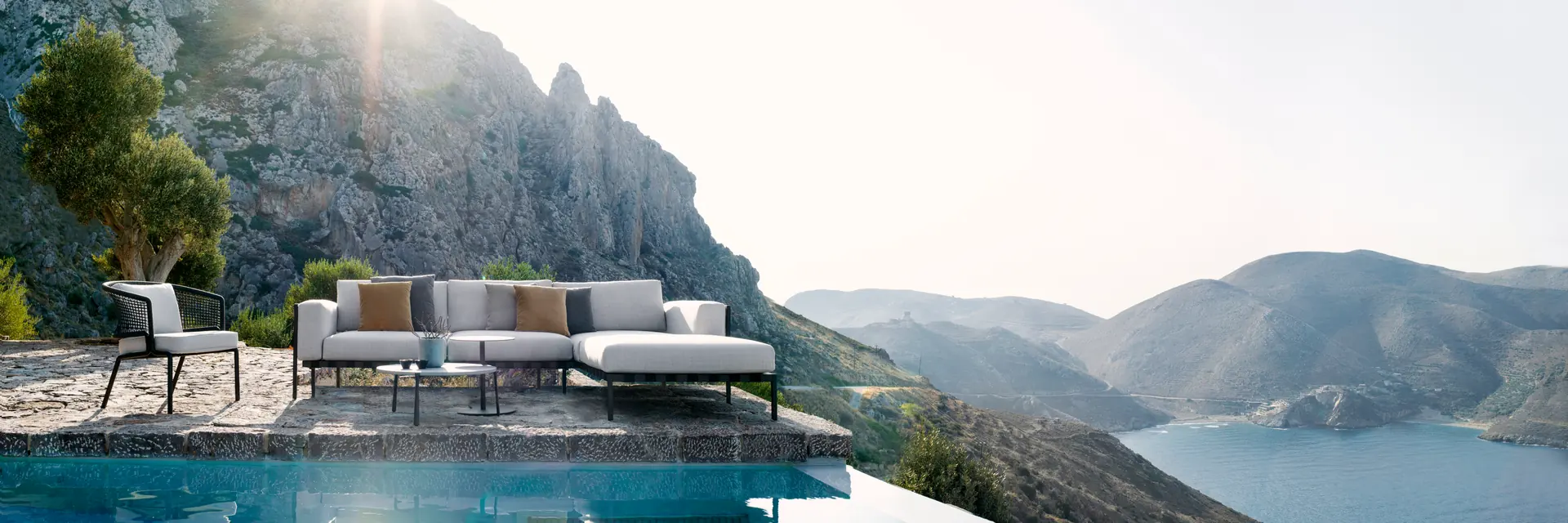 Tribù Natal Alu sofa beside an infinity pool, high above a rocky coast with mountains in the haze