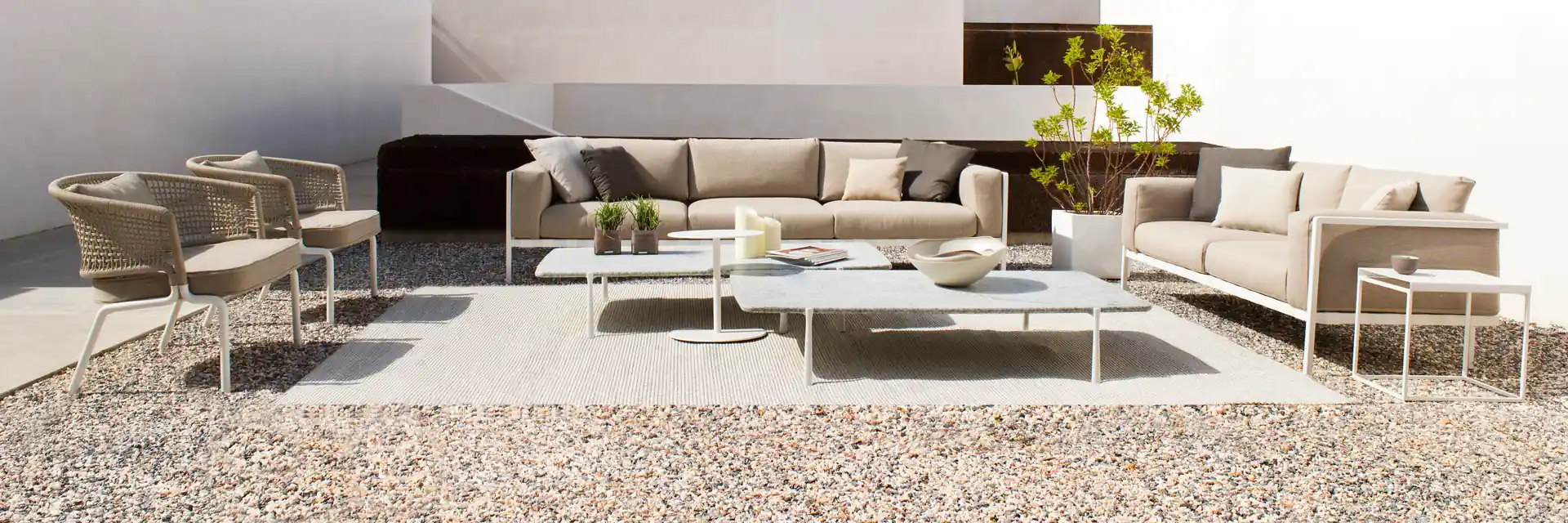 Tribù Natal Alu aluminium sofas, armchairs and low tables on a gravel courtyard between white walls