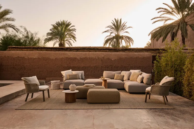 Tribù Nodi sofas, armchairs and coffee tables on a terrace in front of a terracotta wall with palm trees at sunset