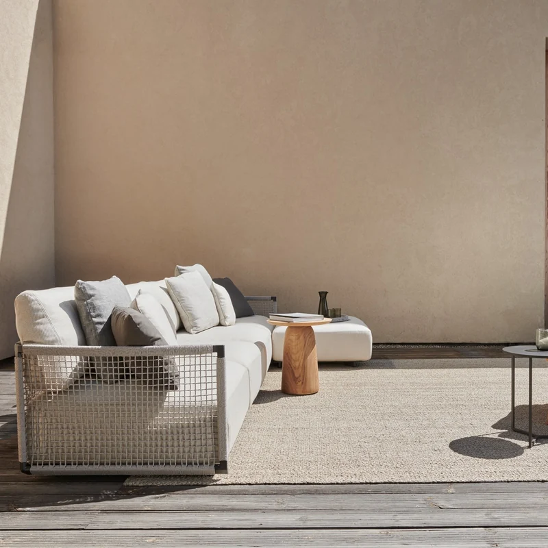 Tribù Nodi sofa with a woven back and side tables on a deck before a sand-colored wall with a wooden door
