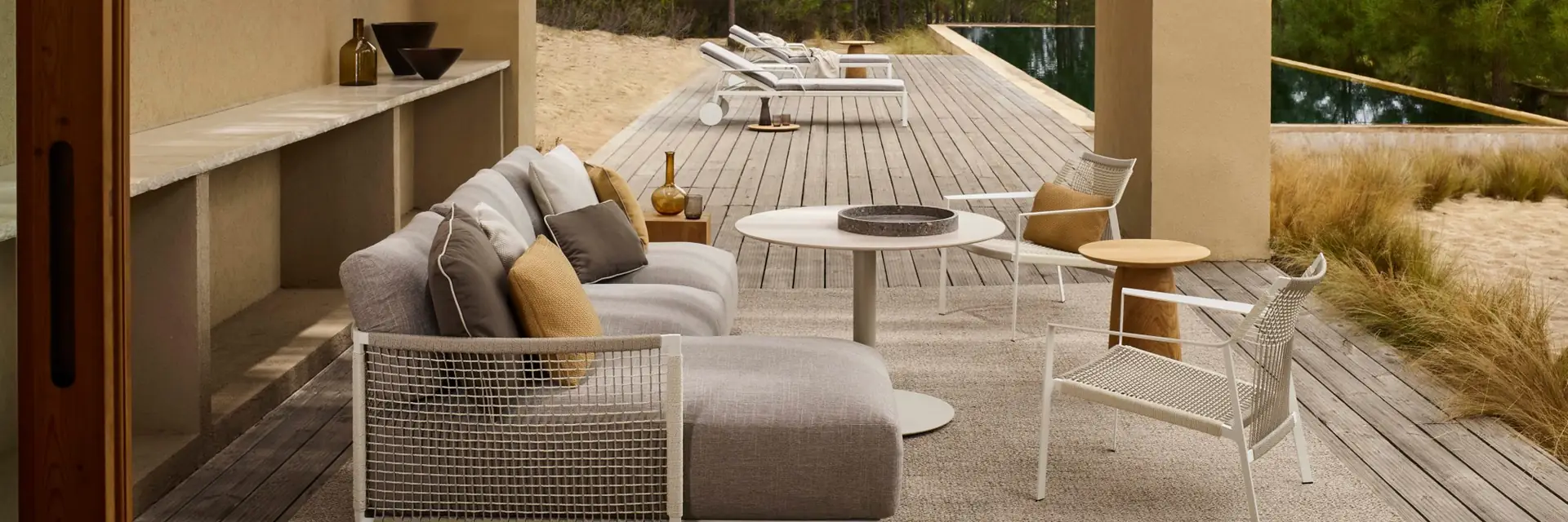 Tribù outdoor sofa and low tables under the timber roof of a covered terrace, with pine trees beyond