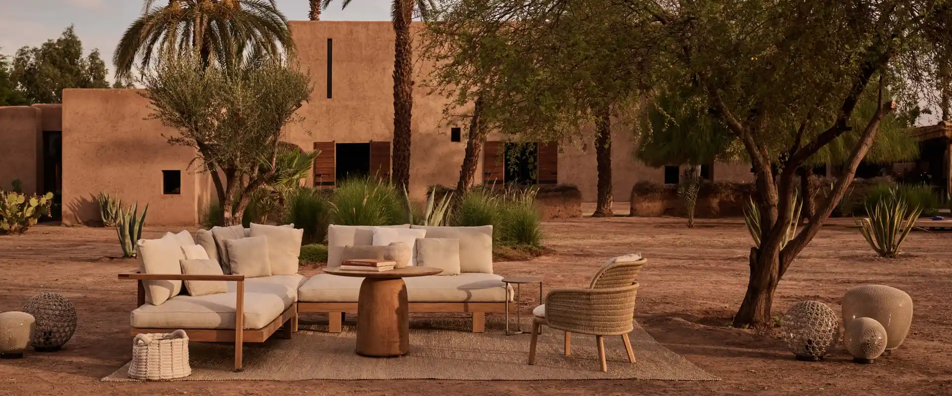 Tribù Pure teak sofas and armchairs on red earth in front of an adobe villa with palm trees