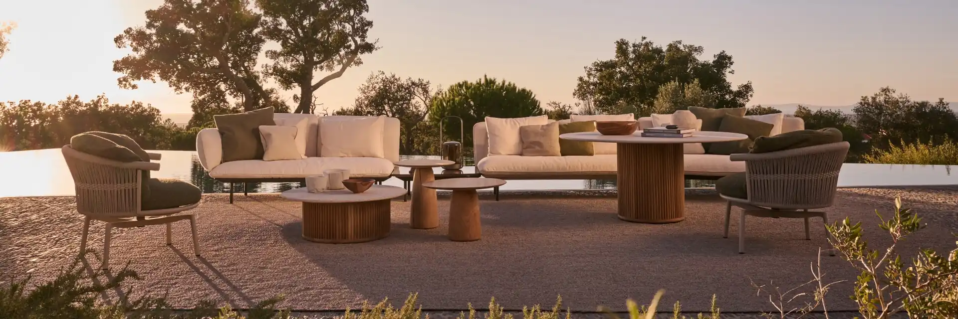 Tribù Senja sofas and lounge chairs around low tables on a terrace at twilight, with trees against a violet sky