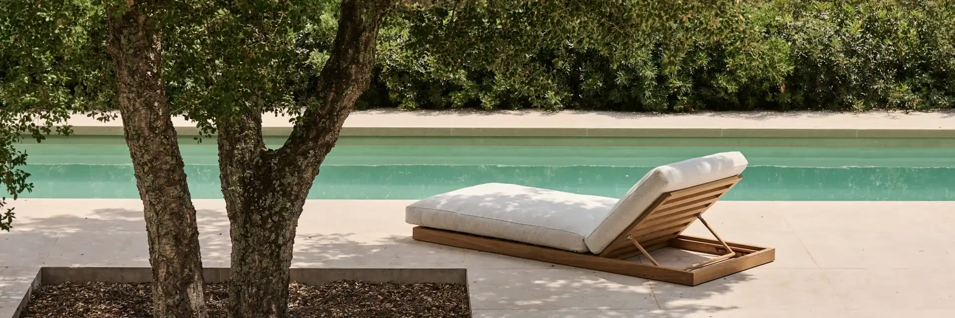 Tribù sun lounger with a white cushion beside a pool, in the shade of a tree