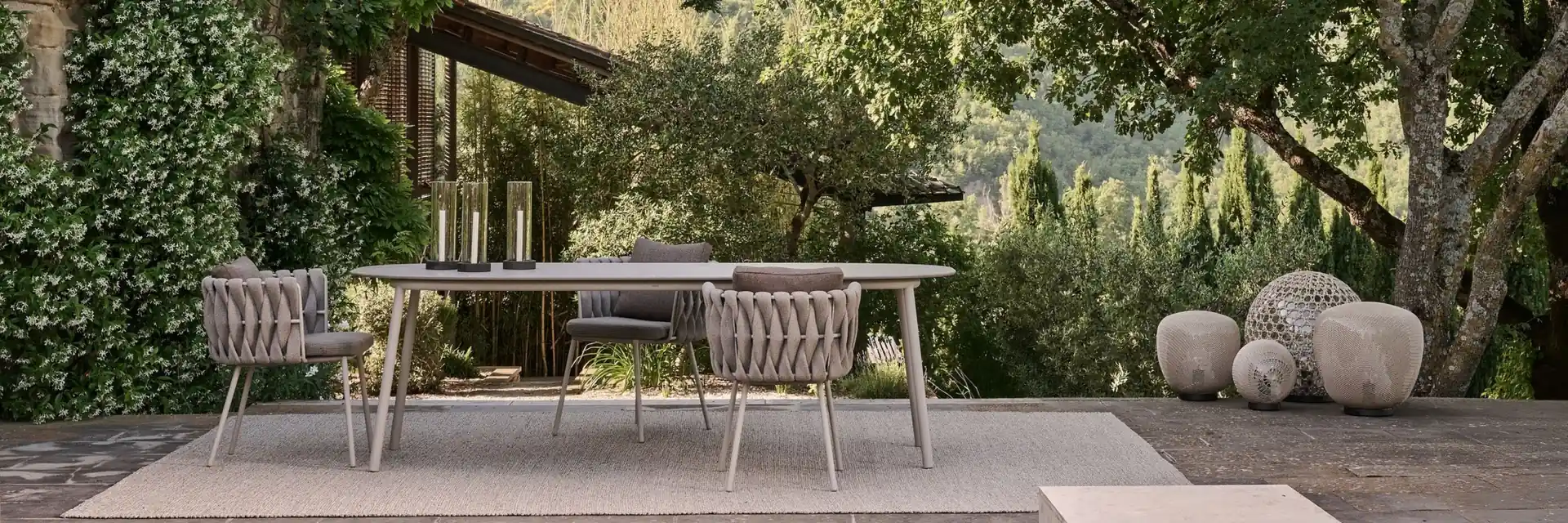 Tribù Tosca rope dining chairs around a pale table on a stone terrace in a green garden