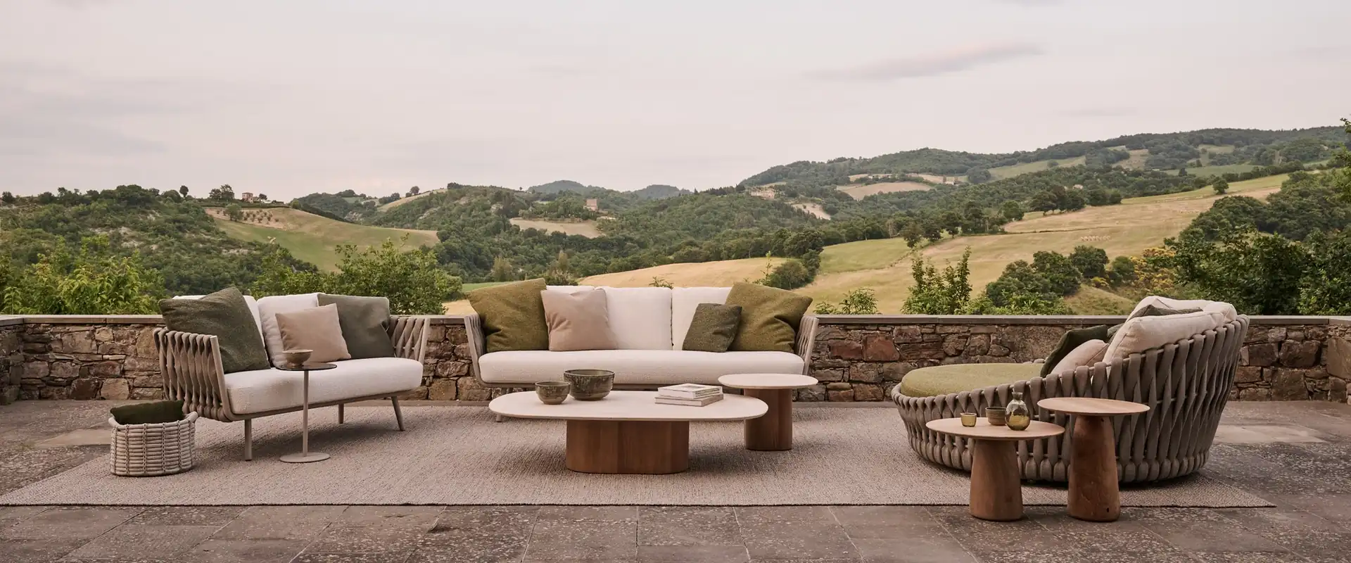 Tribù Tosca sofas, low tables and a round daybed on a stone-edged terrace overlooking rolling hills