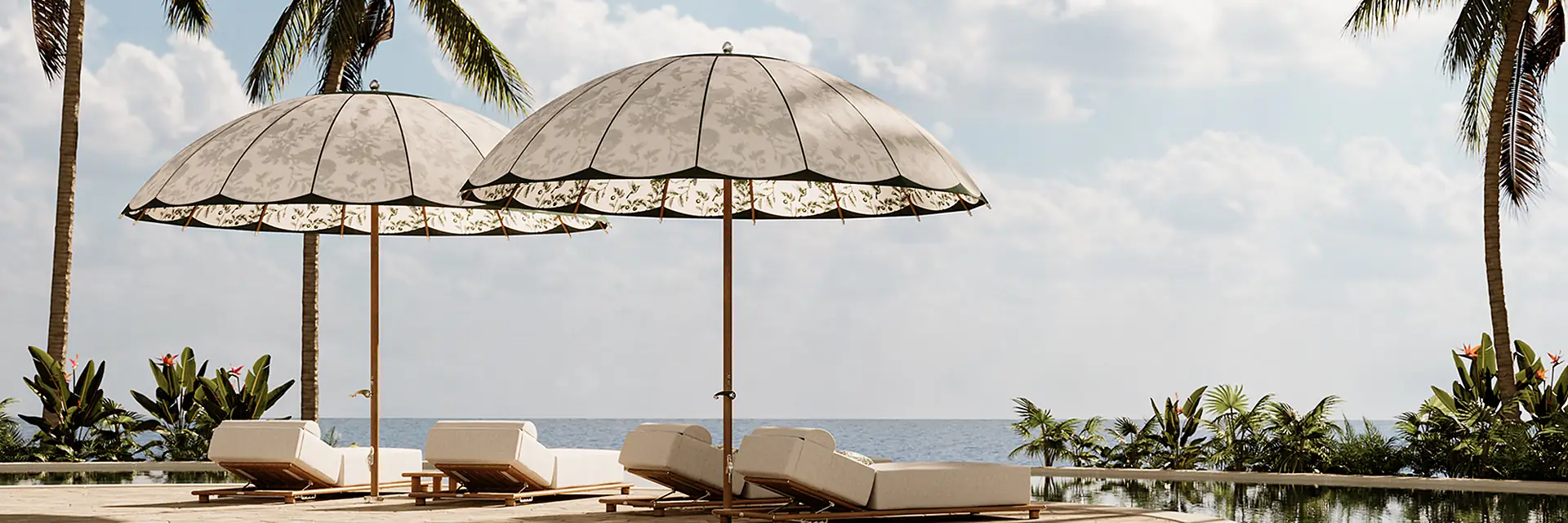 Two dome-shaped Tuuci Bolero parasols with botanical printed canopies over four sun loungers beside an infinity pool, with palm trees and the sea behind