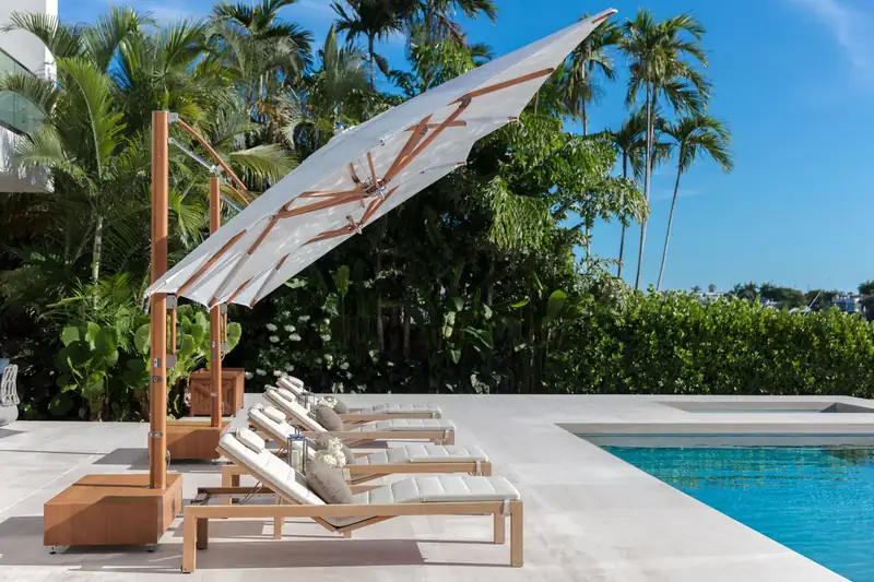 Tuuci Ocean Master MAX cantilever parasol tilted over teak sun loungers beside a pool