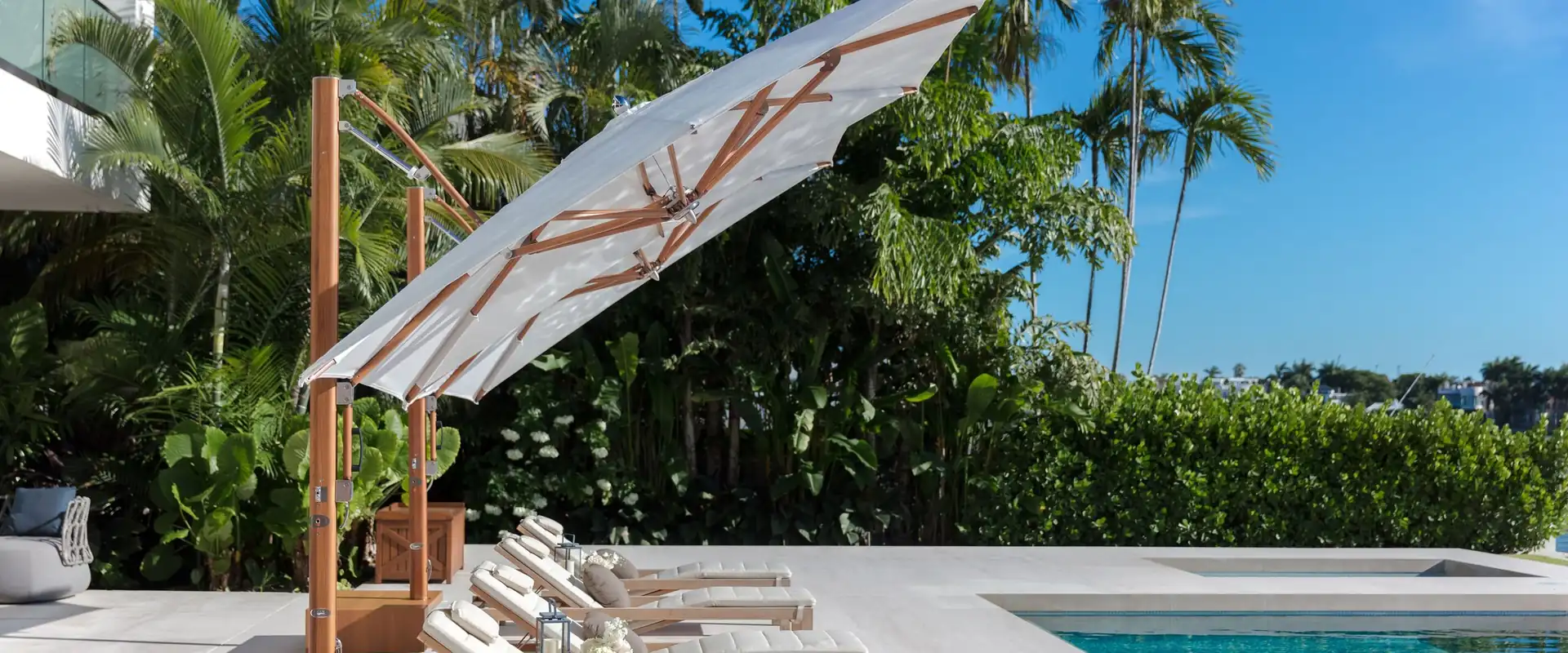 Tuuci Ocean Master MAX cantilever parasol tilted over teak sun loungers beside a pool