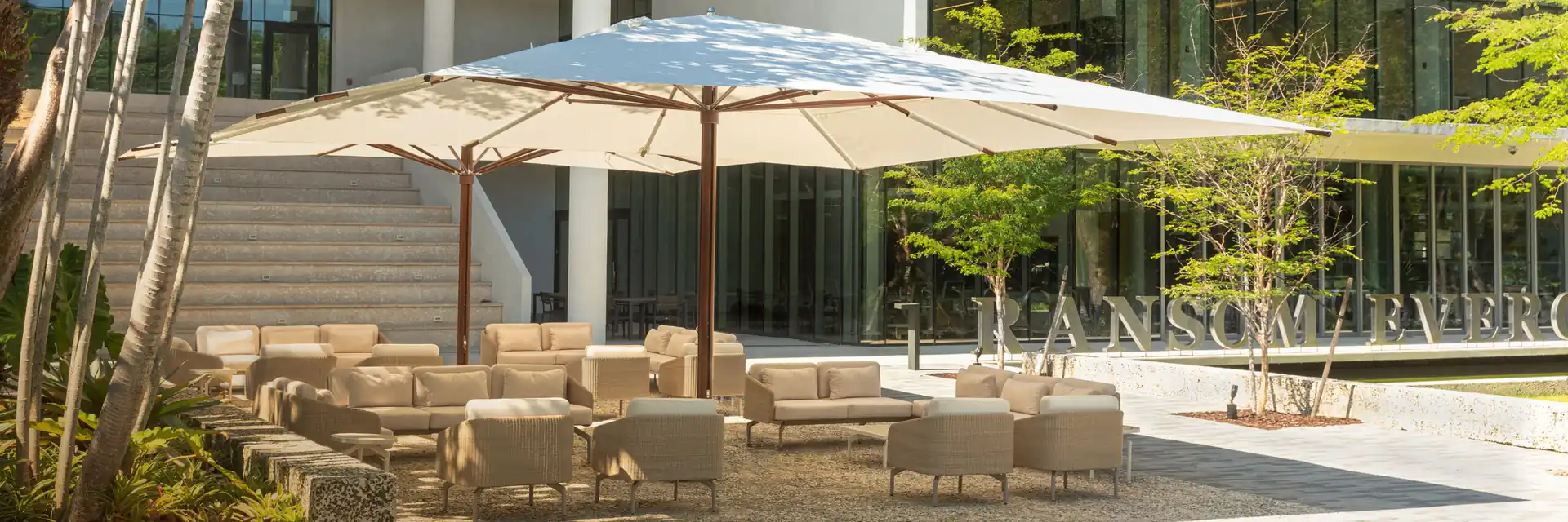 Large white Tuuci Classic parasol with a wood-finish mast over lounge seating in front of a modern glass building