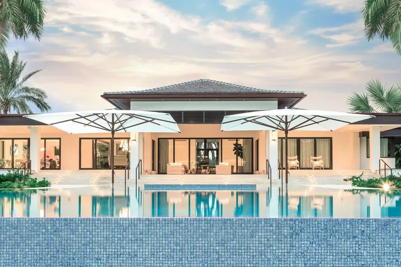 Two white Tuuci Ocean Master MAX Classic parasols in front of a villa across an infinity pool, framed by palms