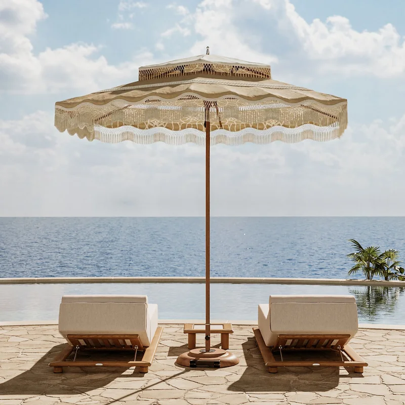 Tuuci Ocean Master M1 Cupola: Bodhi center post parasol with a natural macramé canopy and fringed valance between two cushioned sun loungers on a stone terrace overlooking the sea