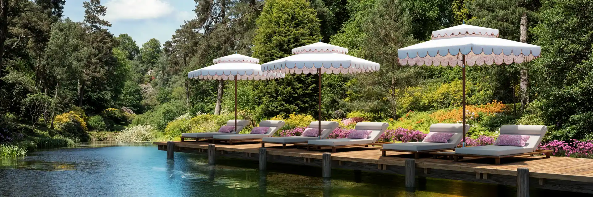 Three Tuuci Ocean Master M1 Cupola parasols with contrast-bound scalloped valances over sun loungers on a wooden deck beside a garden pond, surrounded by tall trees