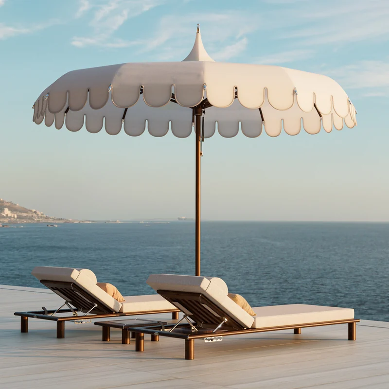 Tuuci Ocean Master M1 Voilare center post parasol with a scalloped cream canopy and pointed top over two cushioned sun loungers on a terrace above the sea
