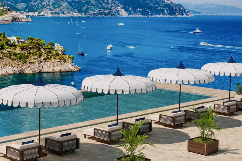 Four Tuuci Ocean Master M1 Voilare center post parasols with scalloped white canopies along a clifftop swimming pool, overlooking a blue bay dotted with boats